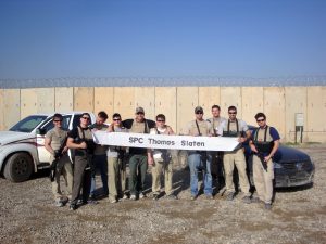 Slaten poses with his unit holding a banner sent to him from an elementary school that “sponsored” him on his deployment.
