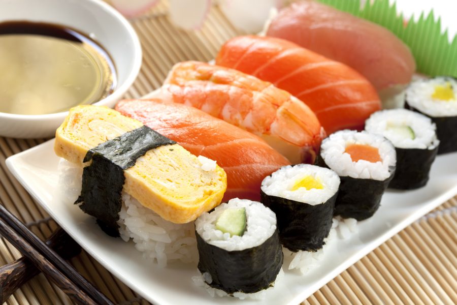 Plate of sushi, with soy sauce and chopsticks, over bamboo background.