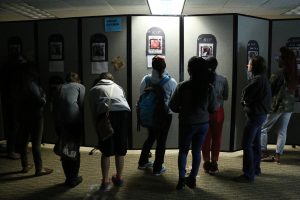 Students pause to look at a wall featuring transgender individuals who have been murdered in the past year in the gender room at Boxes and Walls on Oct. 12.