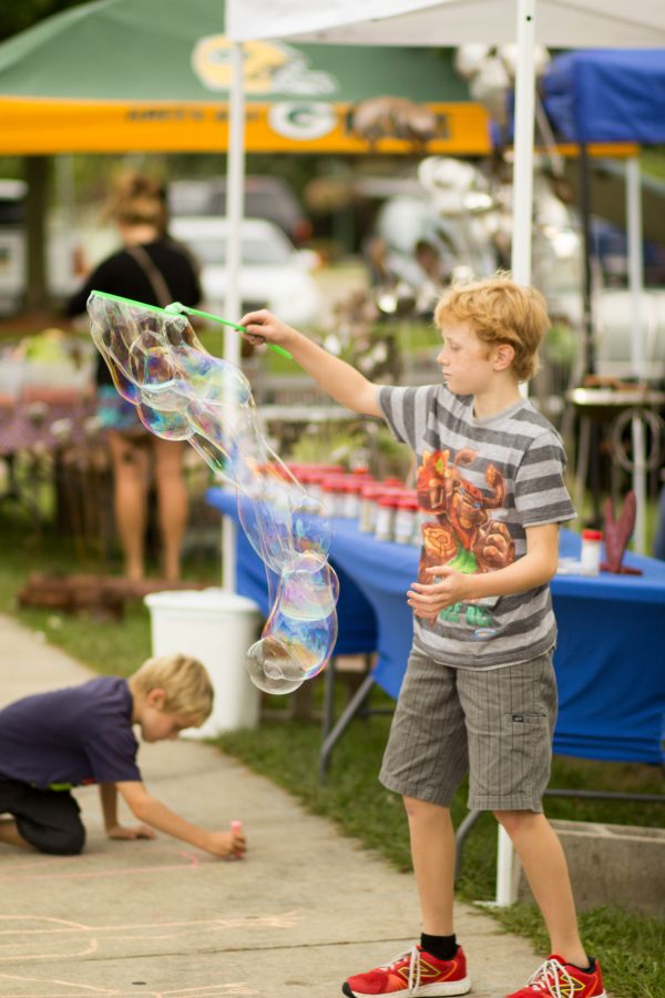 Benjamin McCulloch, son of one of the vendors at the market, uses a bubble wand to create a trail of bubbles. The Whitewater City Market was in full swing on Tuesday, Sept. 8, despite rain clouds looming over. Around two dozen vendors selling produce, jewelry and homemade goods lined Whitewater Street near Cravath Lakefront. Photo by Kimberly Wethal.