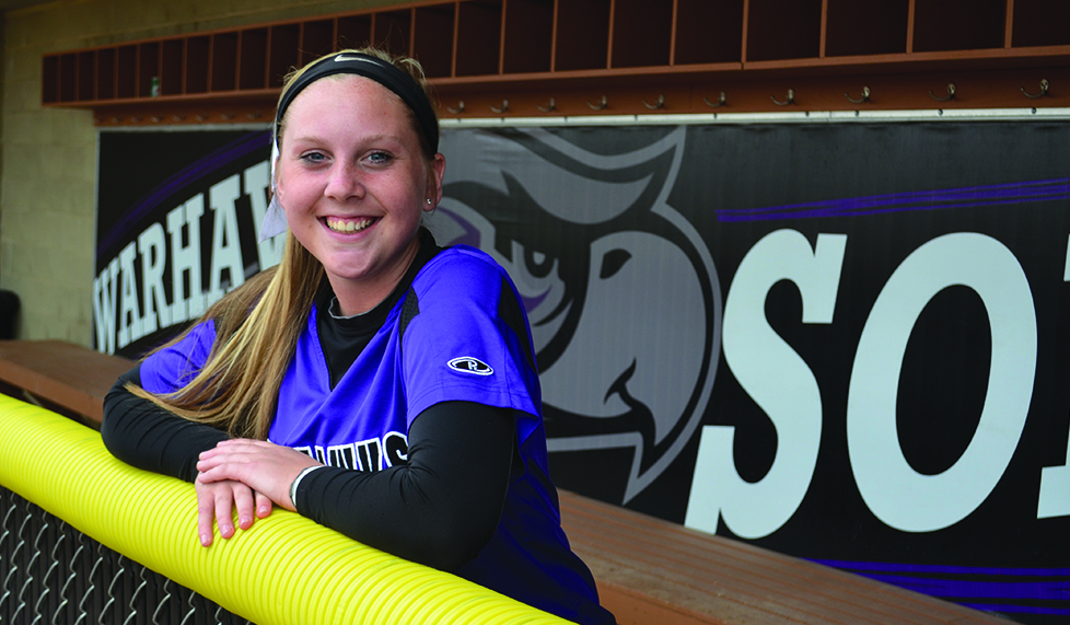Freshman softball pitcher Bella Matthias is all smiles in the Warhawk dugout and on the mound after being near the WIAC lead in every pitching category. Photo by Sierra High