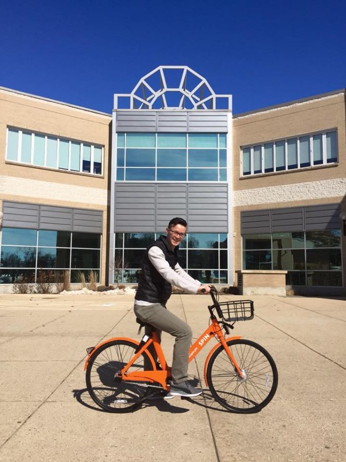 Whitewater Student Government President Tom Kind sits on a Spin ride-share bicycle
