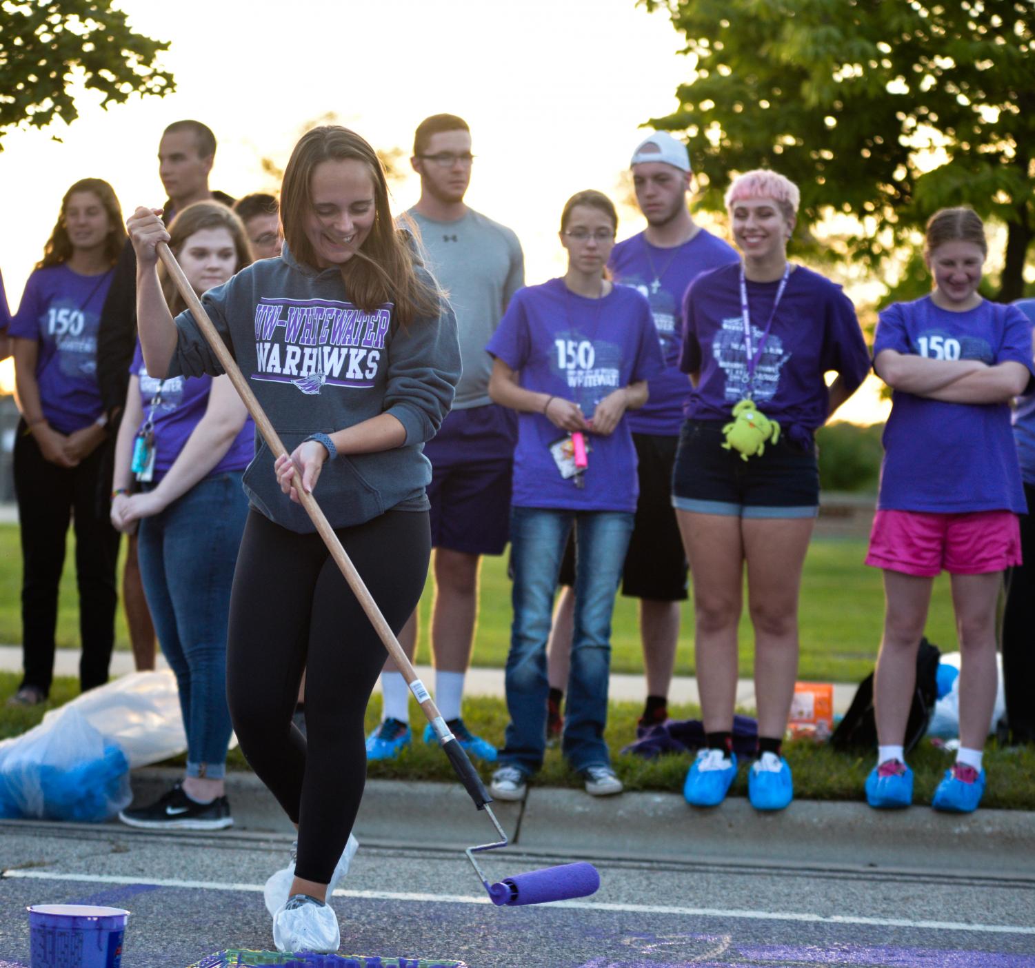 Senior Ally Erck demonstrates how to use a paint roller to freshmen who took part in the tradition of painting Warhawk Drive purple.