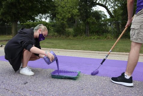 University of Wisconsin-Whitewater student and Hawk Squad member Maddie Neuser (left) adds additional purple paint to a painting tray while Freshman Ryan Waln (right) continues to paint Warhawk Drive nearby.