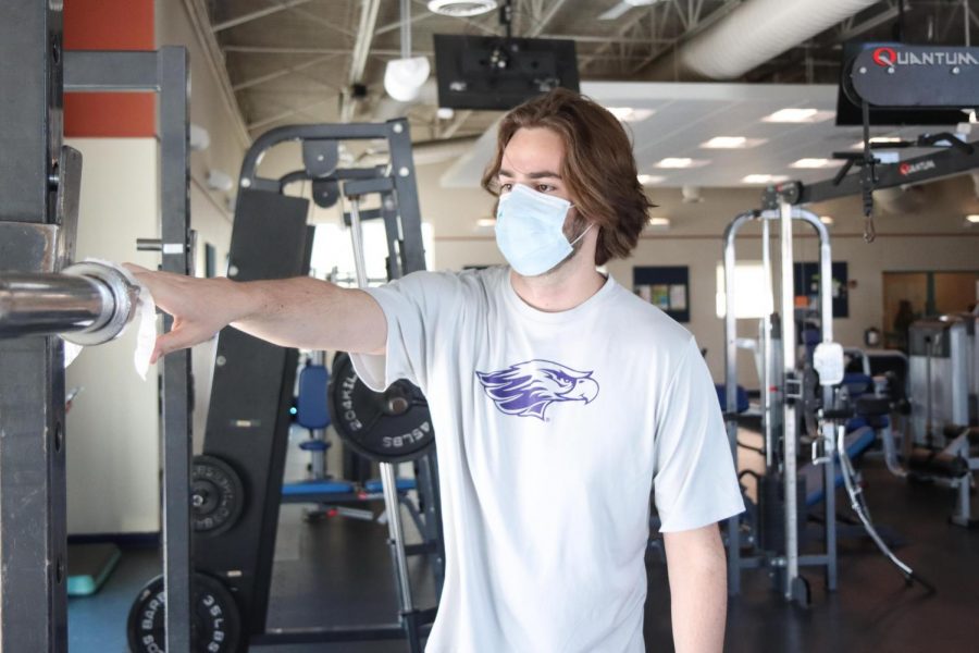 Bennett Andrews, a front desk staff member at the Whitewater aquatic and fitness center cleans
off a barbell shortly after finishing his lift.