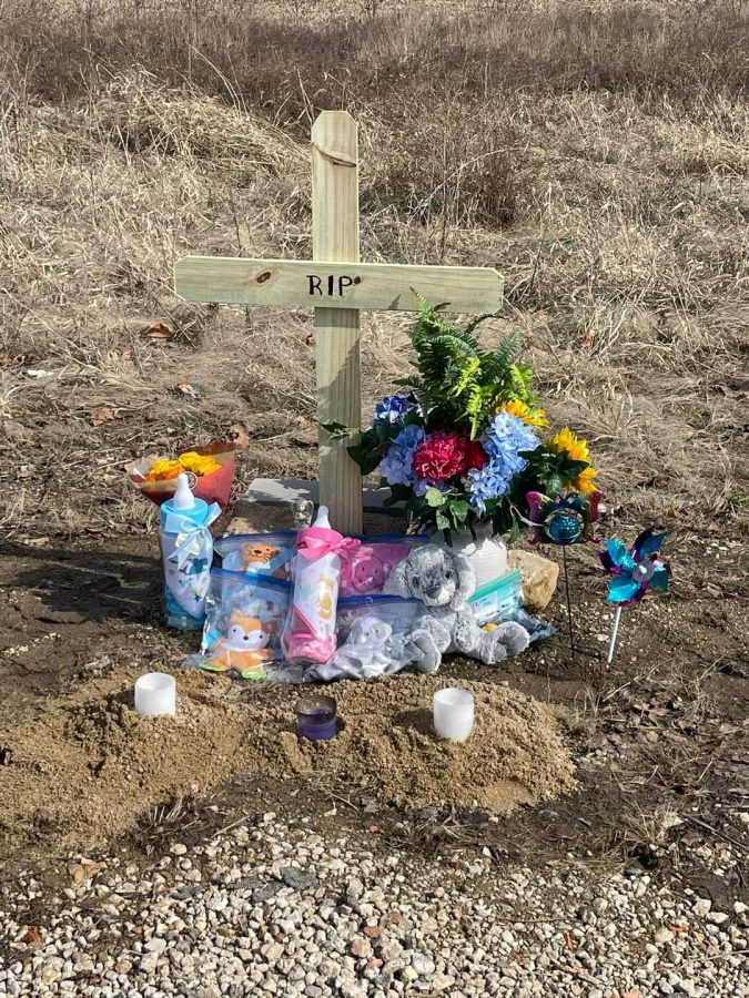 A memorial is seen at Twin Oaks with a cross, candles and baby related items such as bottles and a stuffed rabbit.
