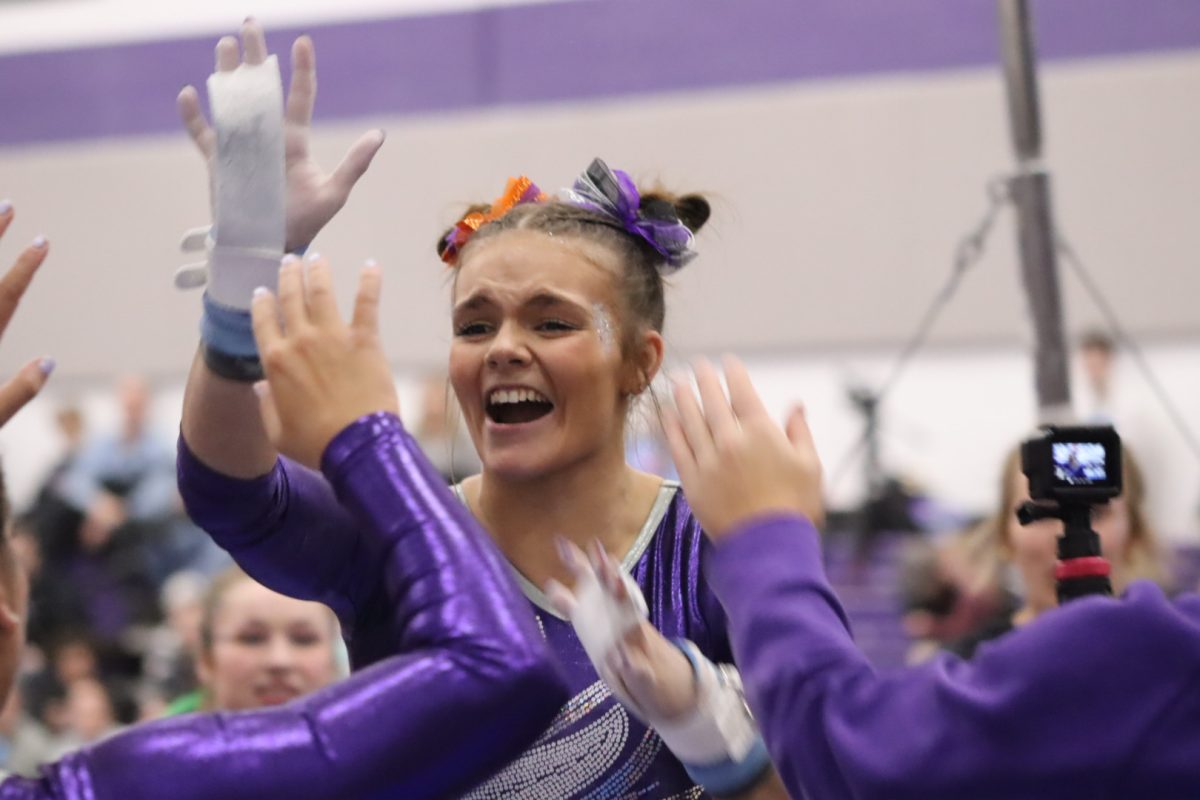 Senior All-Around Gymnast Kelsey Kollhoff high fives her teammates and coaches as she excels at the bars during a home tournament, February 2024.
