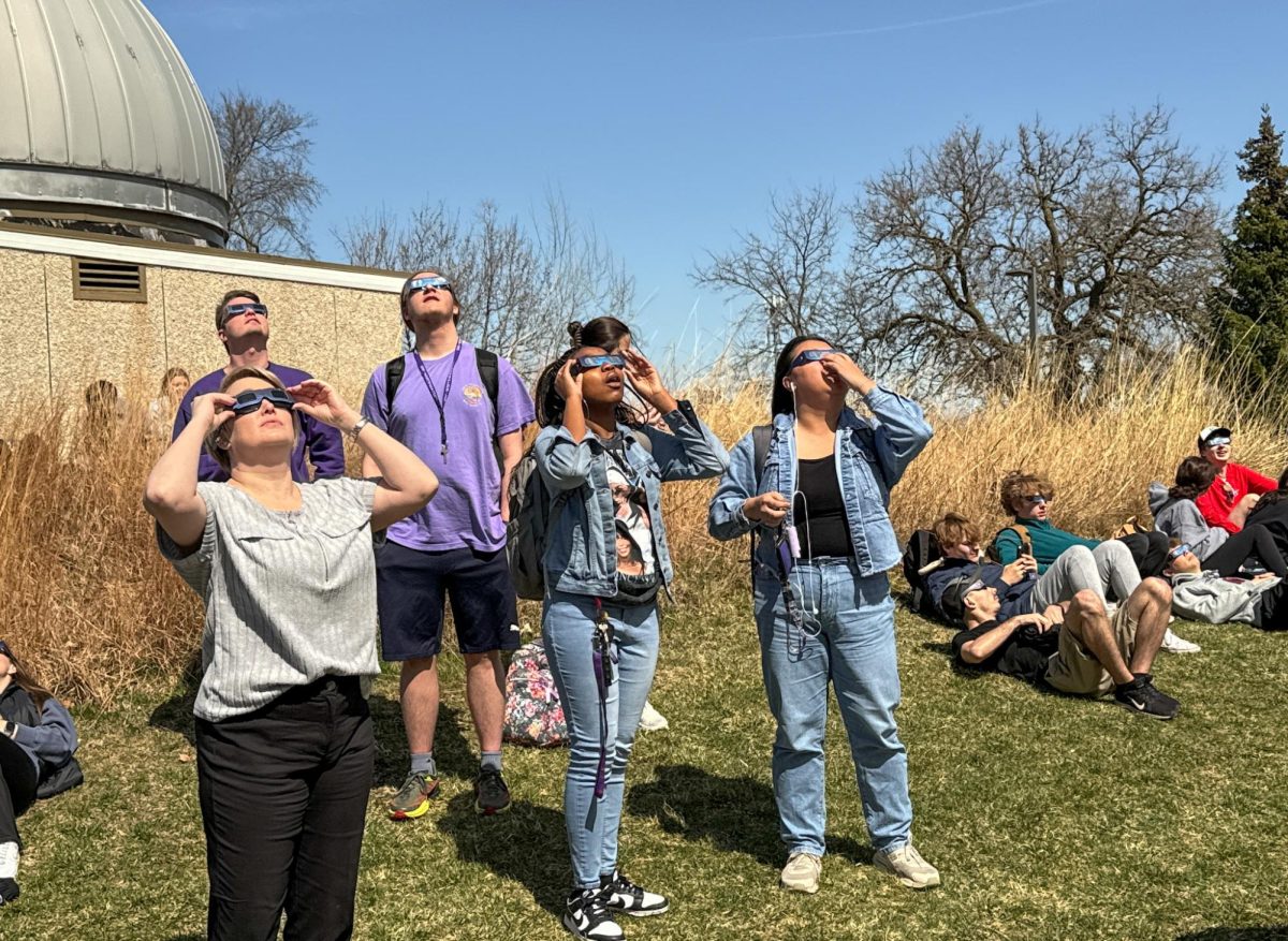 A group of onlookers wearing eclipse glasses gaze up at the Moon passing the Sun outside of the UW-Whitewater Observatory, April 8, 2024.