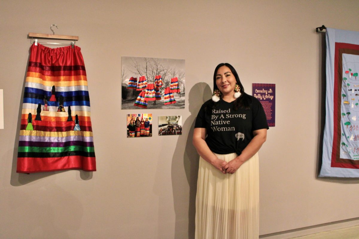 Featured artist, Agnus Yellow Bear, standing next to her artwork (seven sister skirt) at the Crossman Gallery in the center of the arts, on Wednesday, September 18.