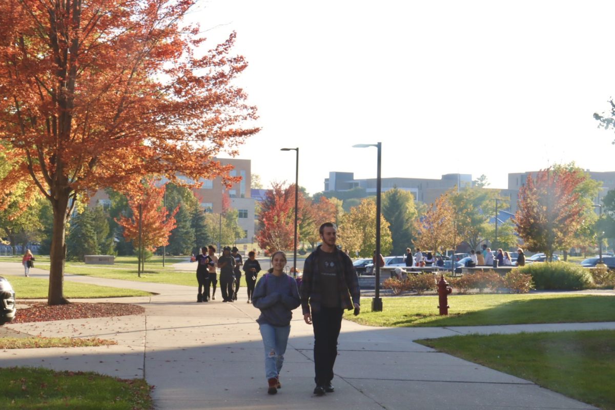 Students stroll along the sidewalk near Goodhue Hall in the evening amongst the fall leaves, October 2024.