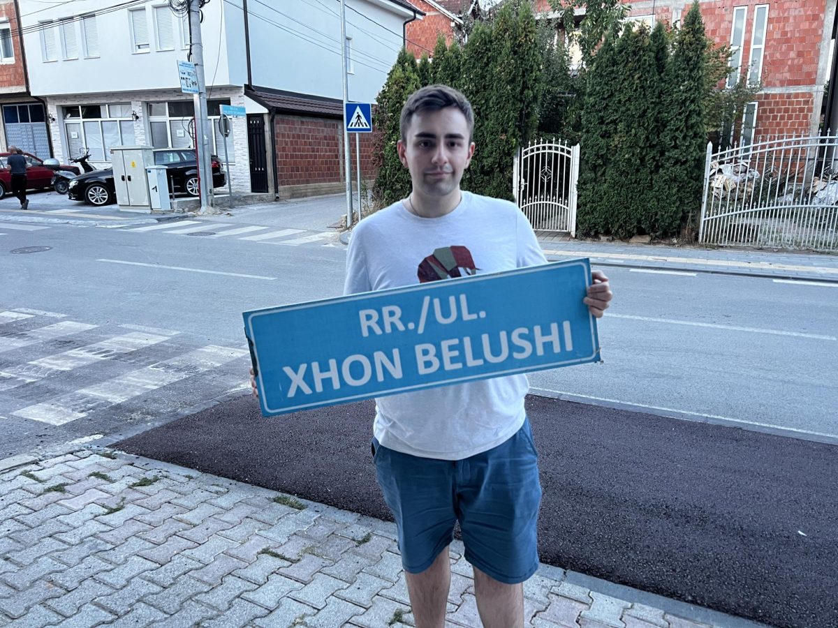 Bleron Grajçevci holding the "John Belushi Street" sign (Spelled "Xhon Belushi" in Albanian) in Podujeva, Kosova