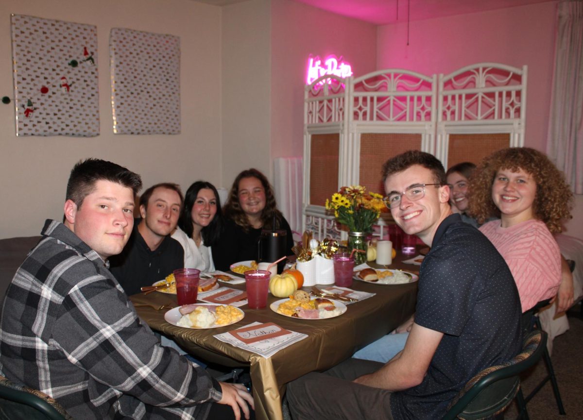 A group of friends posing for a group photo around the dinner table for a Friendsgiving meal on a off-campus apartment. From left to right, Nathan Rea, Senior, Mitchell Flora, Sophomore, Hailey Battersby, Junior, Amy Londo, Senior, Kasey Aucutt, Senior, Anna Heddinger, Junior, and Evan Christman, Senior. 
