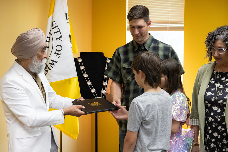 UW-Oshkosh Chancellor Manohar Singh hands a diploma to Barry Moodie, as his children Emmett and Kate and his late wife’s mother, Mary Altenburg, look on. (UW-Oshkosh)