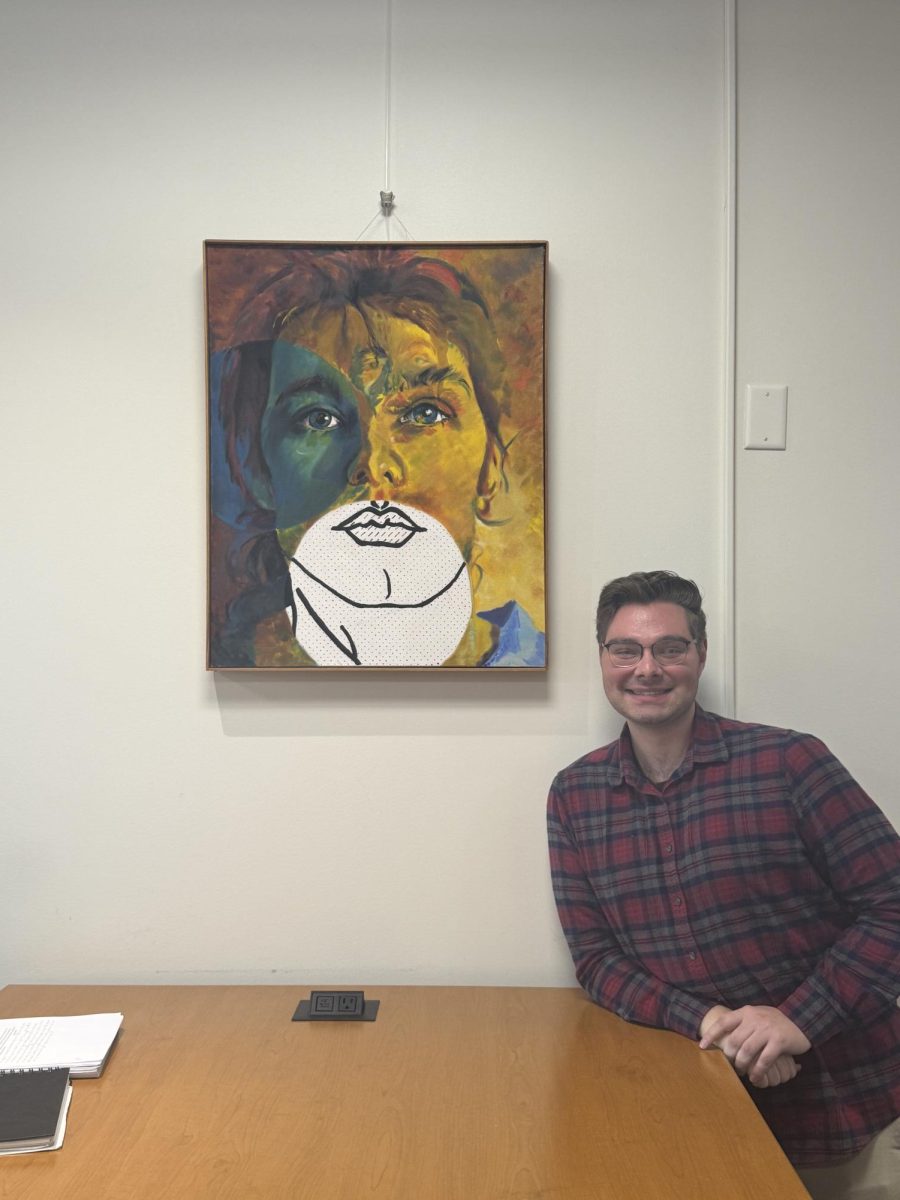 Anton Saucedo smiling in front of his father’s self-portrait that he did when he was a college student.
