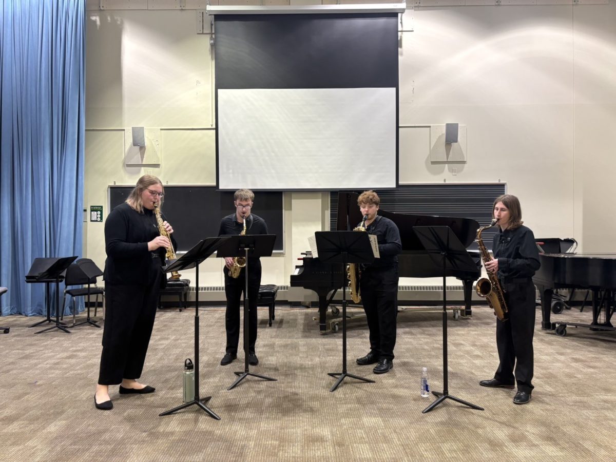 Mitchell McCarty is seen playing with his quartet for the conference on the far right, holding and playing the tenor saxophone.
